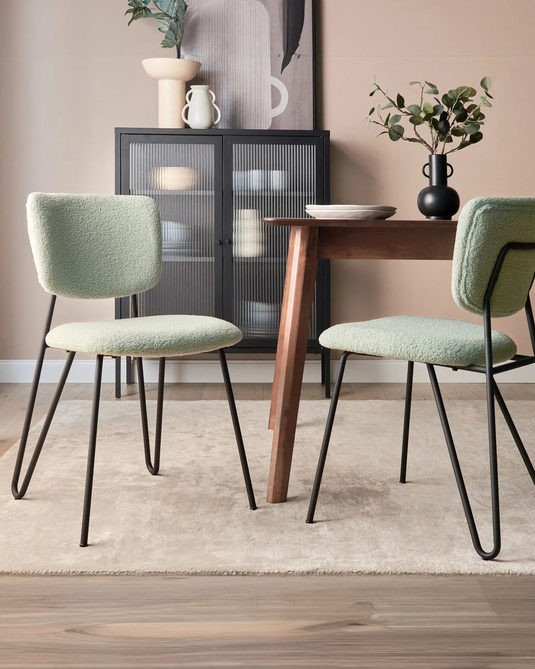 Modern dining room featuring soft green bouclé chairs, a warm wood dining table, and sleek black accents.