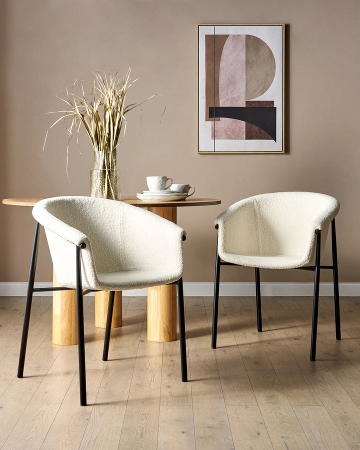 White bouclé dining chairs styled around a wood dining table in a warm, contemporary dining space.
