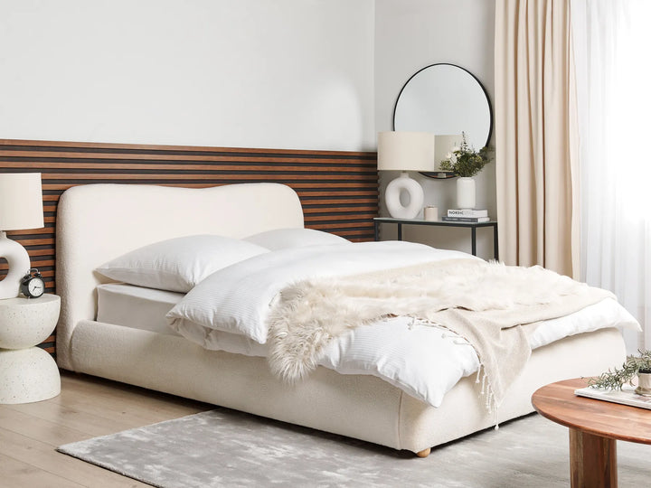 Neatly made bed with white bedding and a wooden headboard in a bedroom setting.