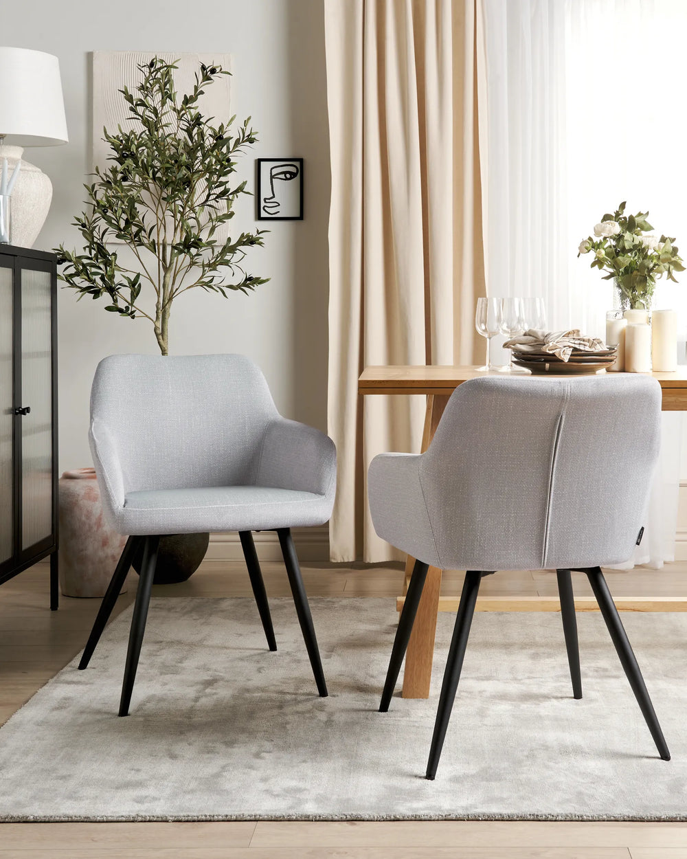 Light grey velvet dining chairs with rounded backrests and slanted black metal legs around a dining table in a contemporary dining space with modern décor.