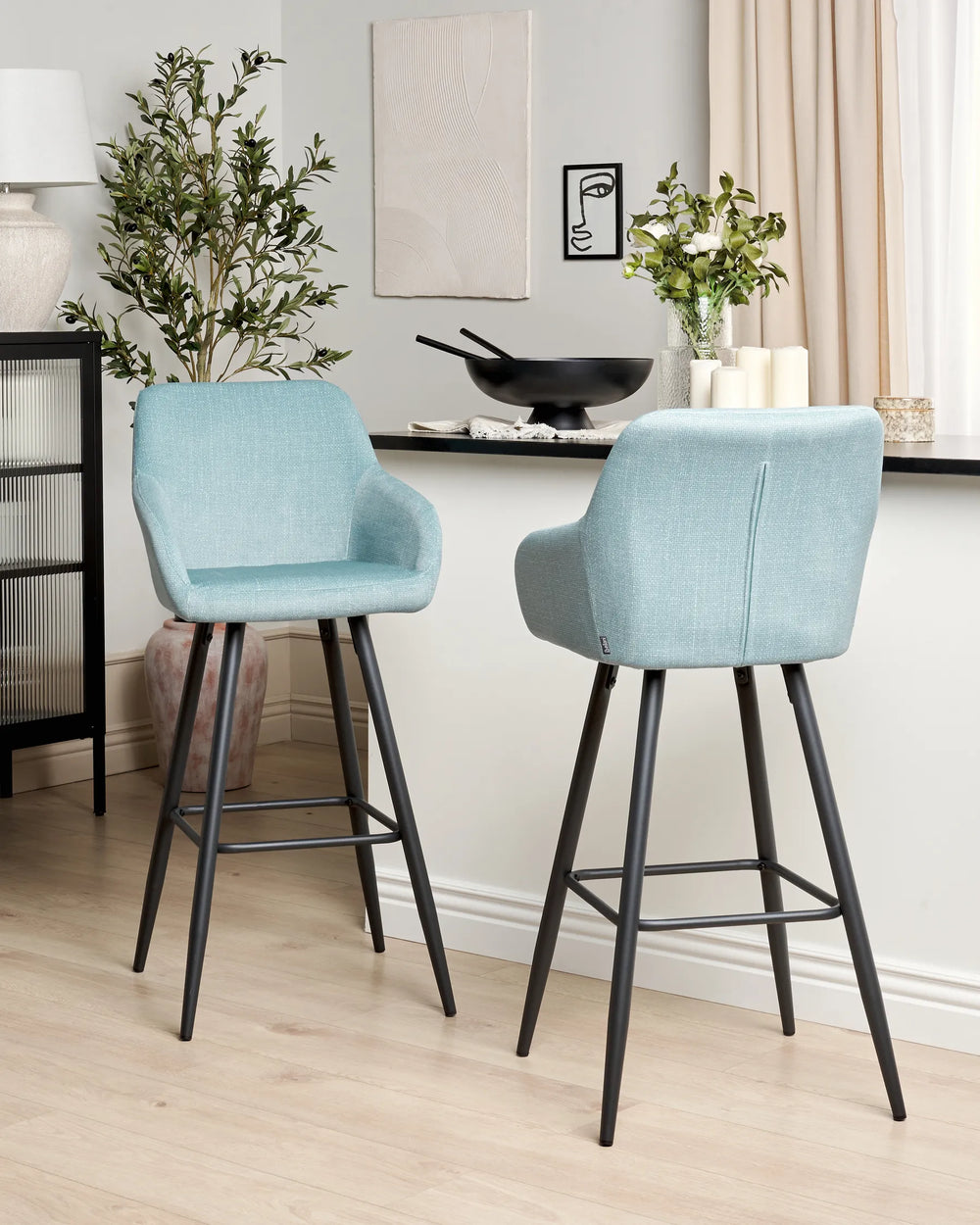 Light blue velvet bar chairs with rounded backrests and slanted black metal legs around a bar counter in a contemporary kitchen or dining space with modern décor.