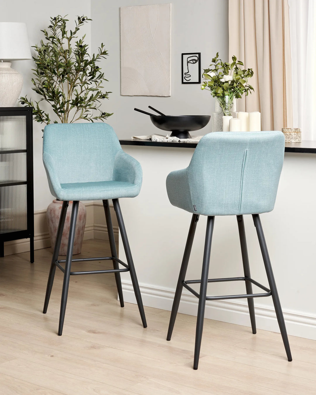Light blue velvet bar chairs with rounded backrests and slanted black metal legs around a bar counter in a contemporary kitchen or dining space with modern décor.