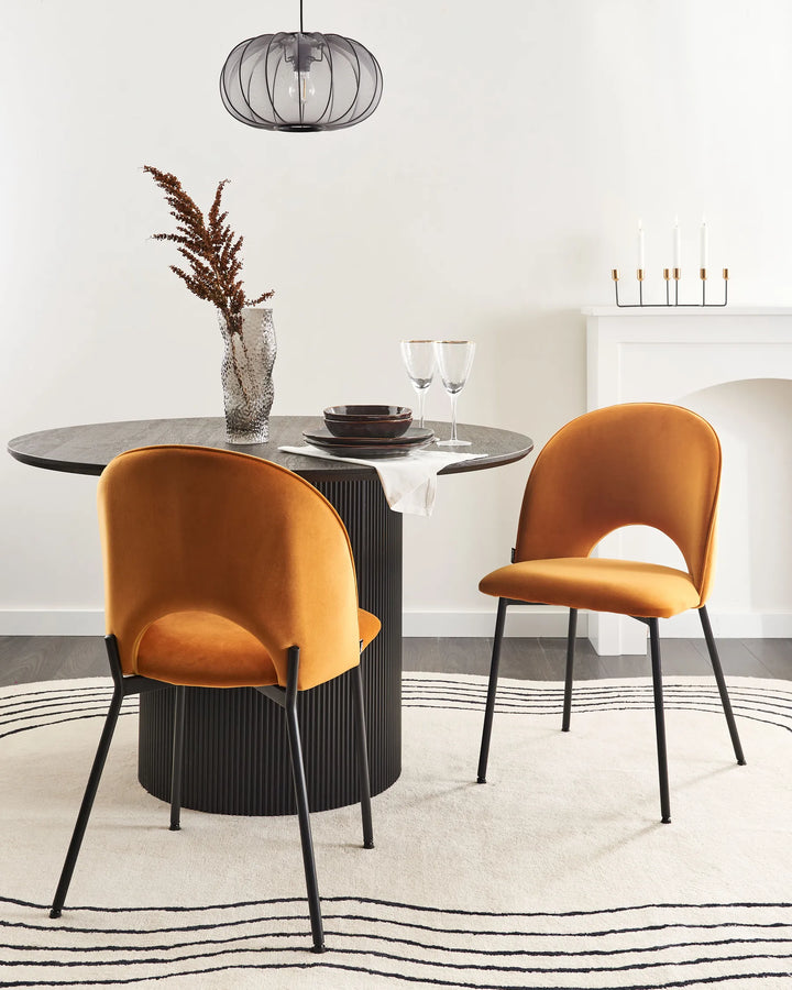 Elegant dining space featuring mustard velvet chairs around a black pedestal table, adding warmth, contrast, and modern sophistication.