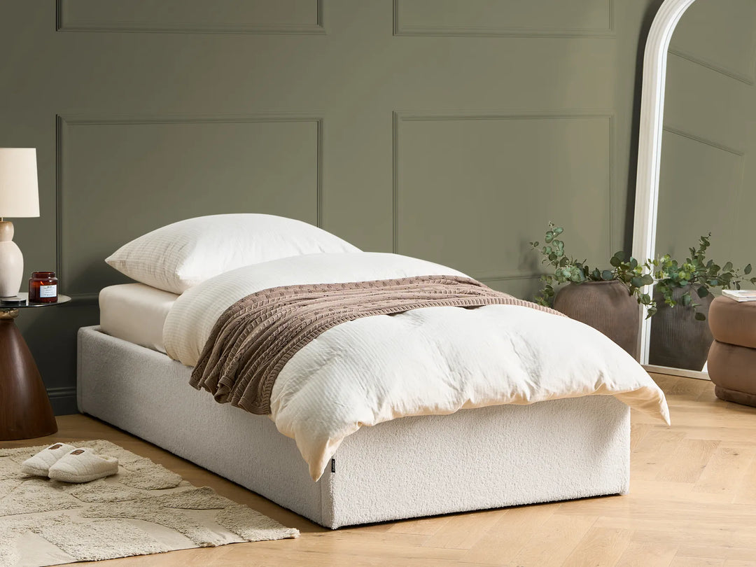 White bed with brown blanket in a room 