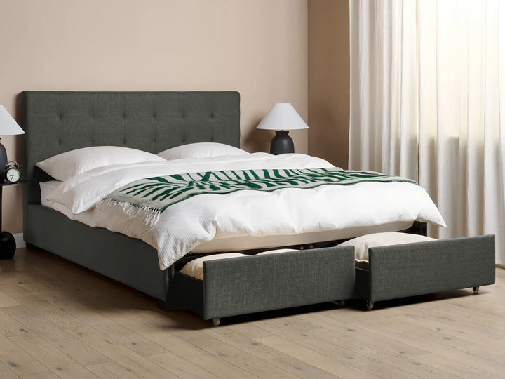 Gray upholstered bed with white bedding and a green blanket