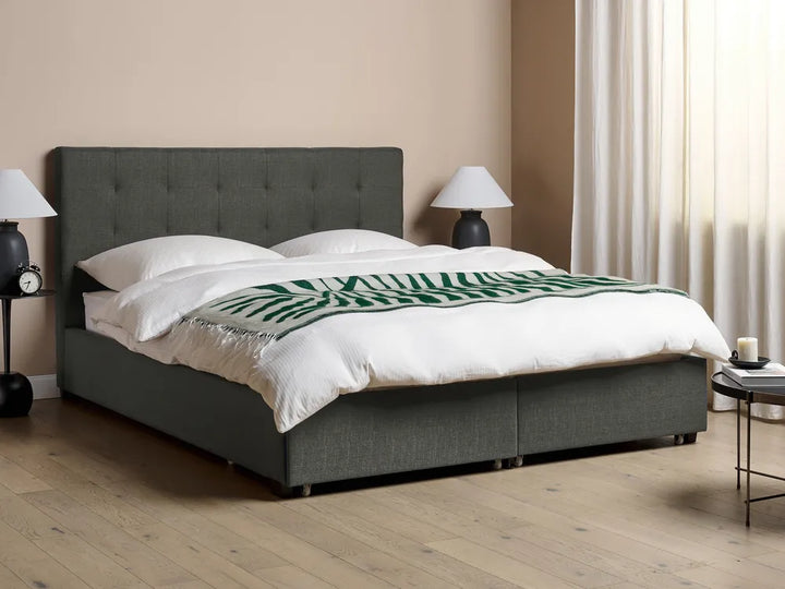 Gray upholstered bed with white bedding and a green patterned throw 