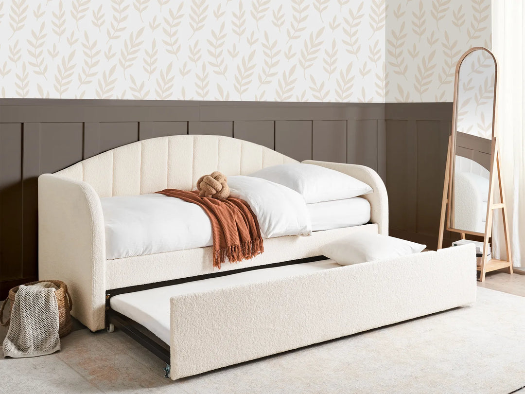 White upholstered bed with storage drawers in a room with patterned wallpaper.