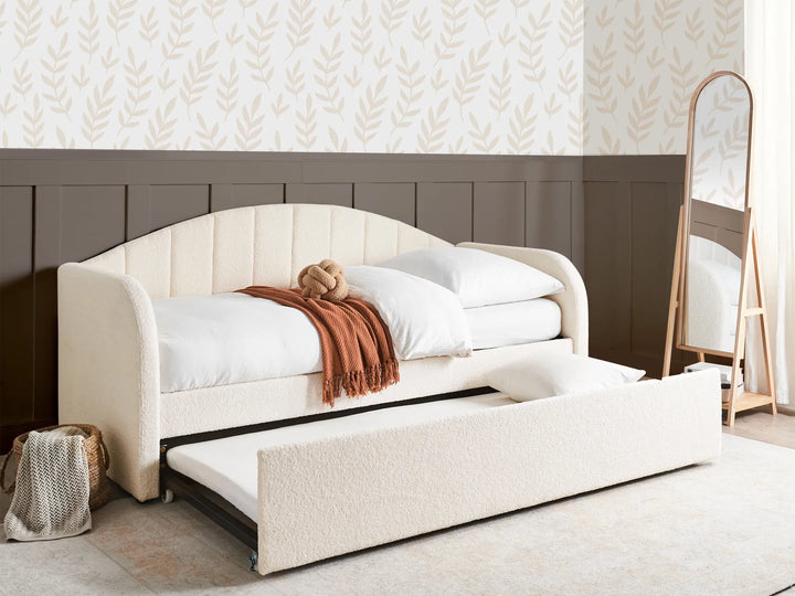 White upholstered bed with storage drawers in a room with patterned wallpaper.