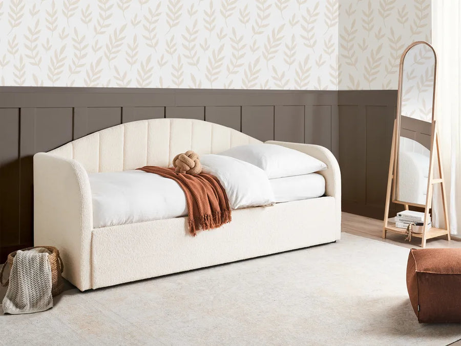 White upholstered bed with white bedding and a brown blanket in a room with patterned wallpaper.
