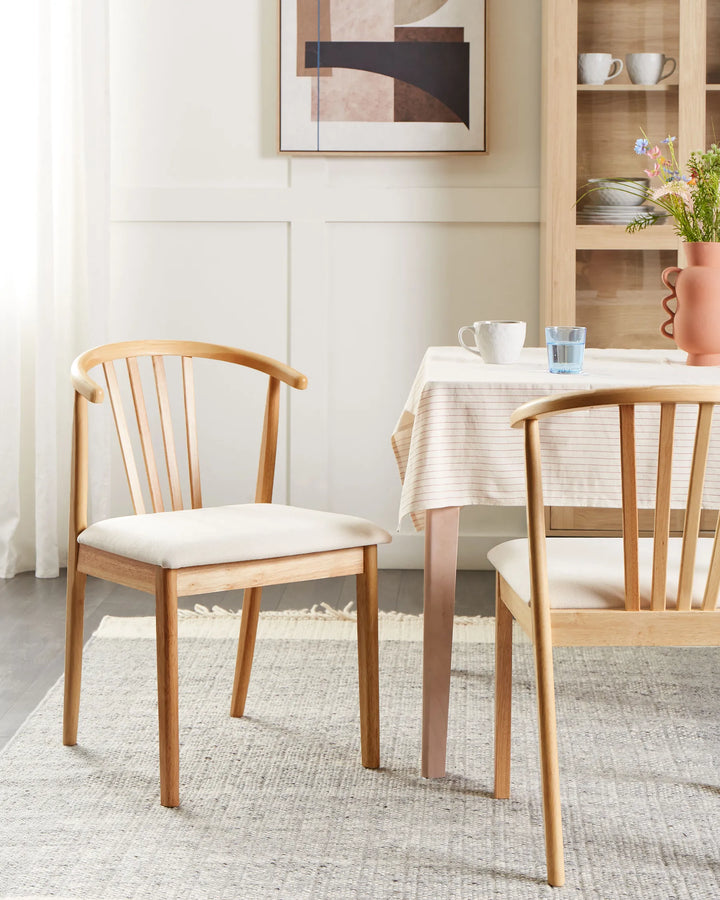 Light wood dining chairs with cream upholstered seats around a dining table in a bright dining room.
