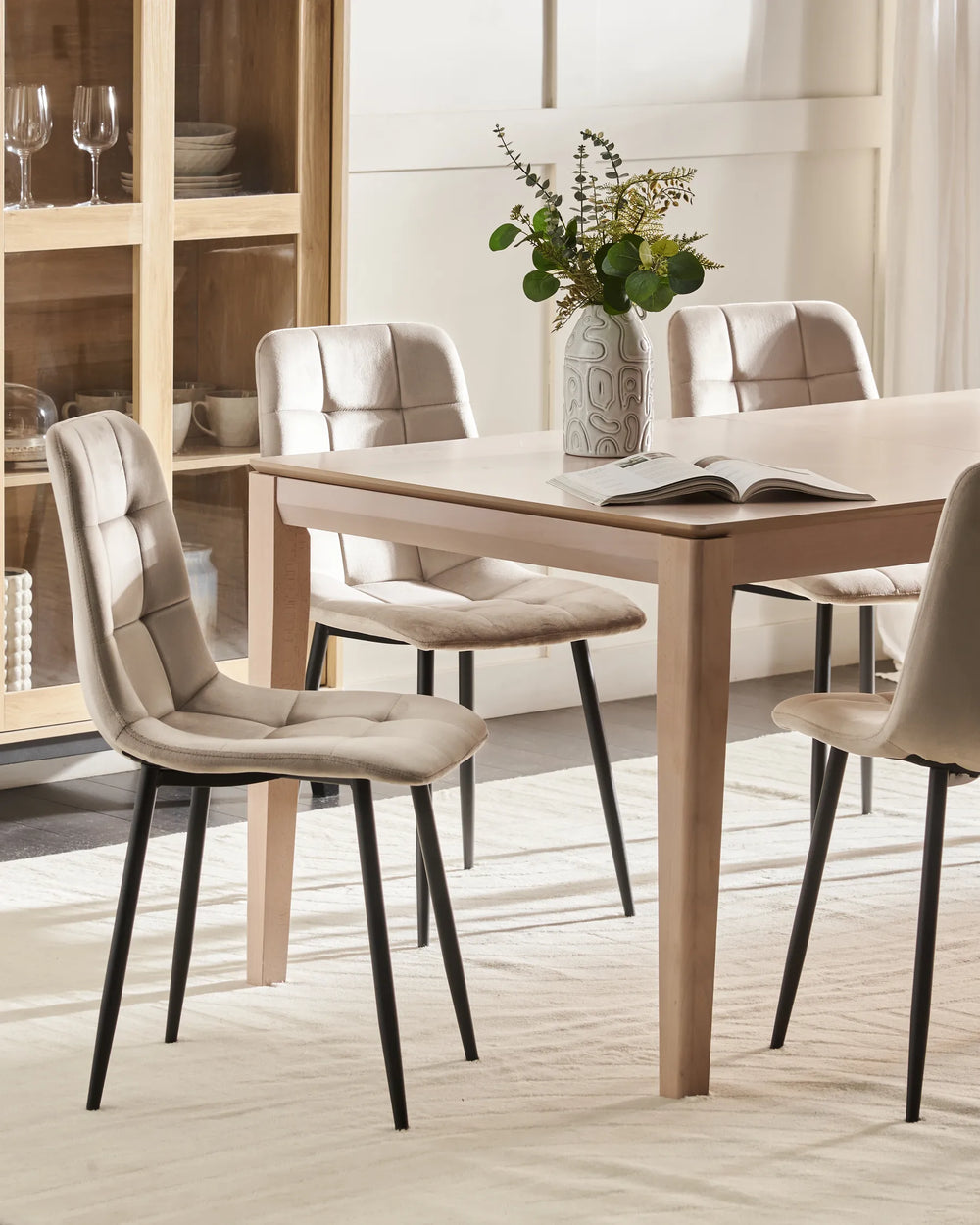 Light-filled dining room featuring beige velvet chairs around a natural wood table, creating a warm, sophisticated, and contemporary setting.