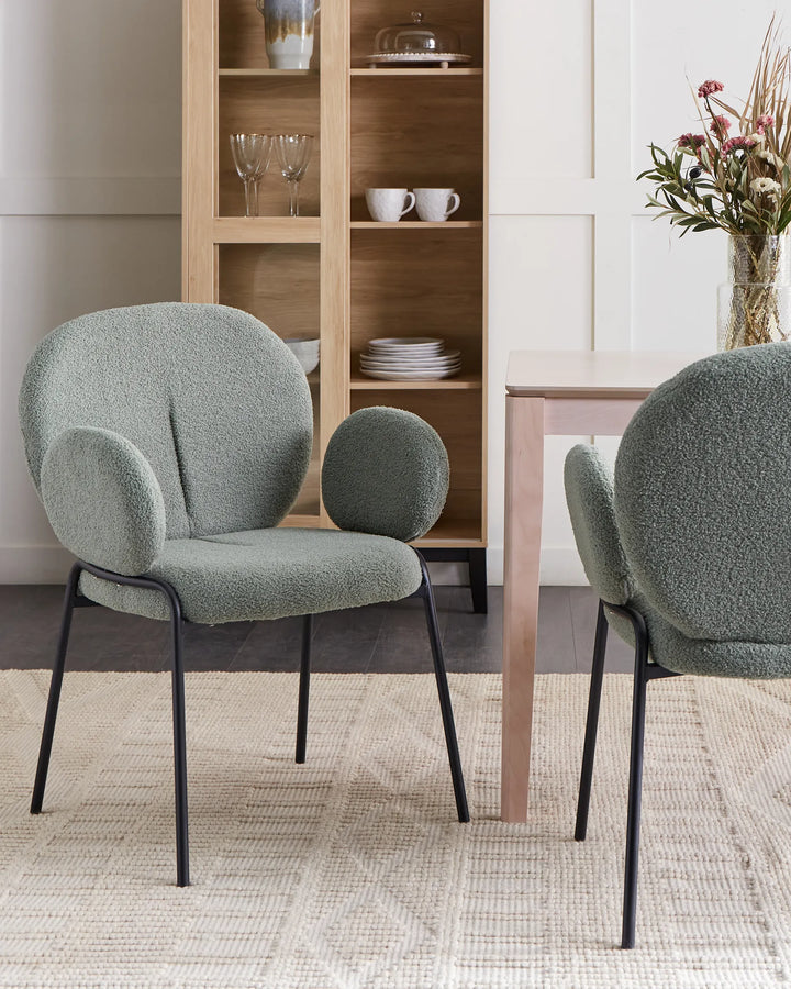 Light green bouclé dining chairs with tall curved backrests and black metal legs around a dining table in a bright, modern dining space with minimalist décor.