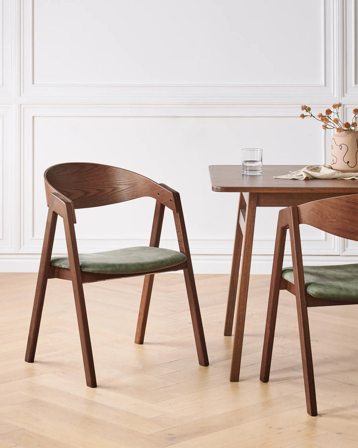 Dark wood dining chairs with green upholstered seats around a wooden dining table in a modern dining room.