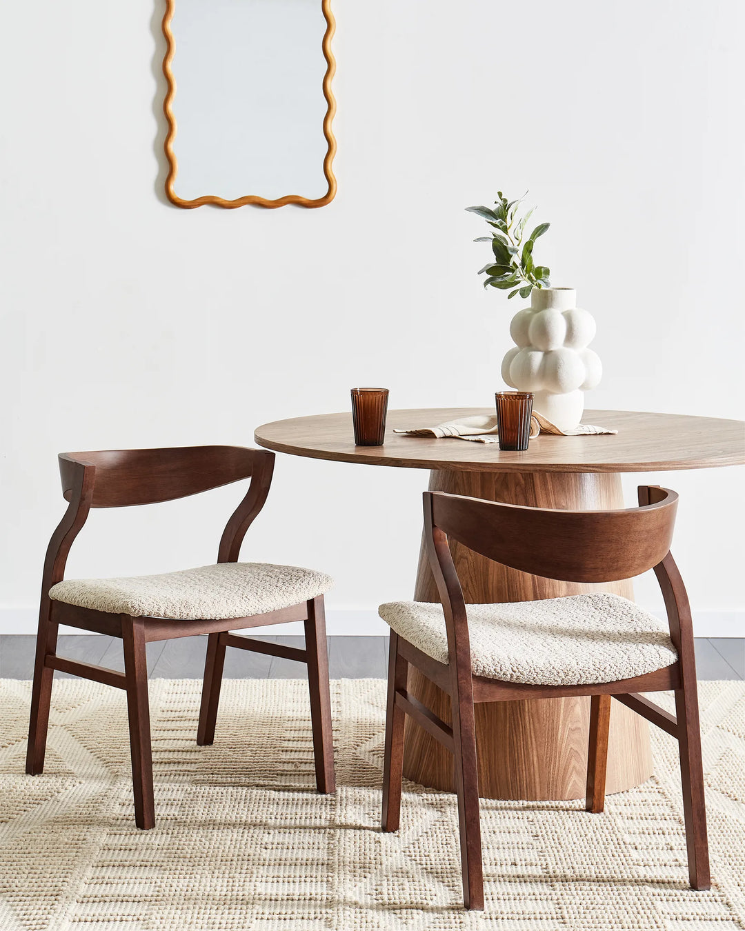 Walnut dining chairs with soft textured cream upholstery styled around a round wooden dining table in a warm, minimalist dining space featuring neutral décor, sculptural accents, soft natural tones, and cozy contemporary styling.