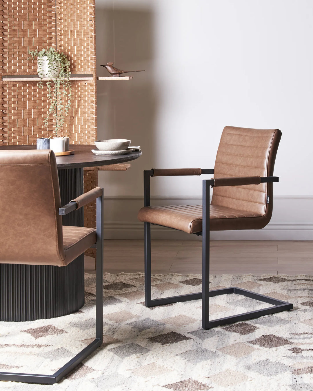 Styled around a modern dining table, these brown faux leather cantilever chairs bring warmth and character to the space. The combination of rich upholstery, black metal framing, and clean architectural lines creates a sophisticated industrial-modern dining atmosphere.