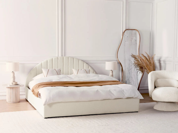 Modern bedroom with a white bed, lamp, and chair against a light-colored wall.