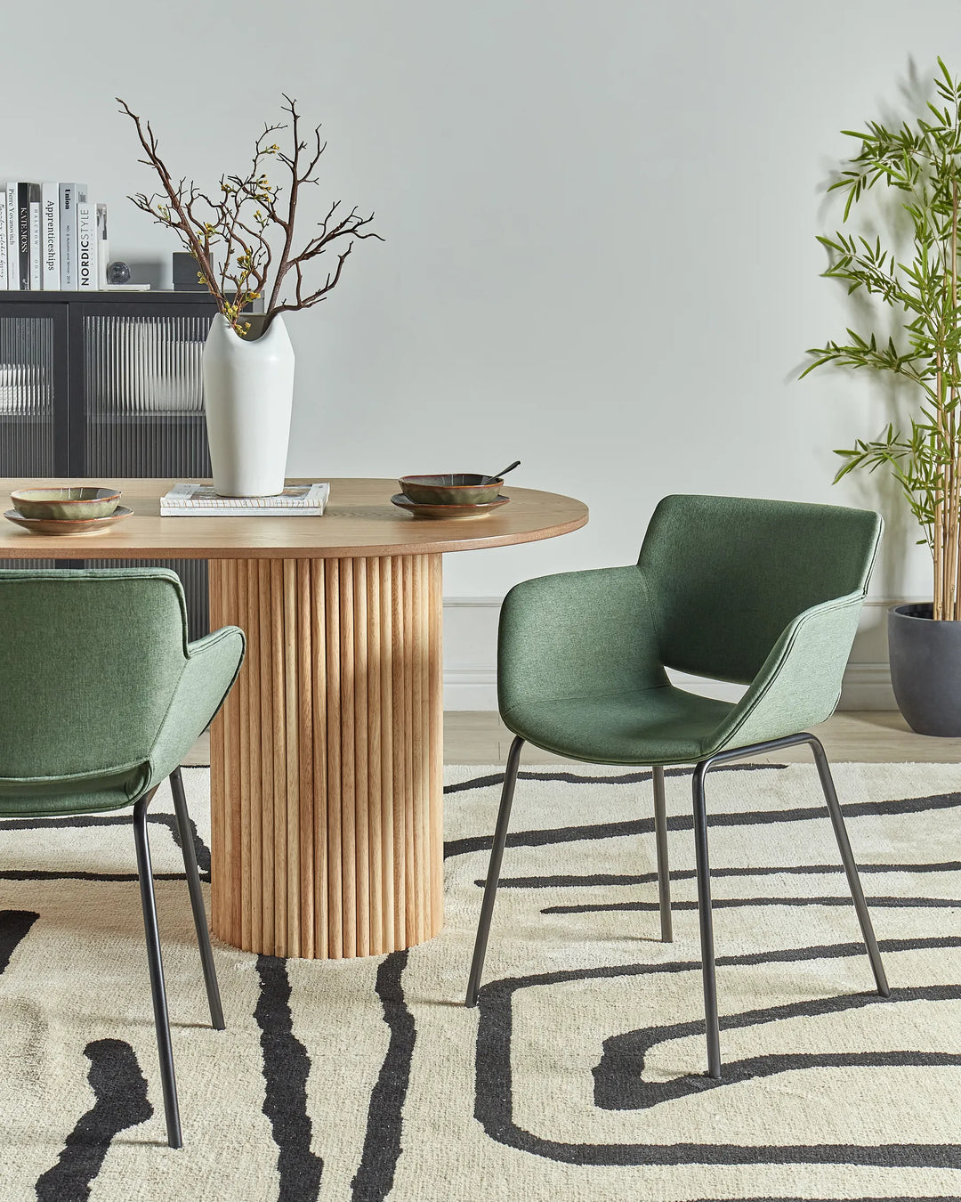 Green fabric dining chairs with integrated armrests and black metal legs around a dining table in a contemporary dining space with modern décor.