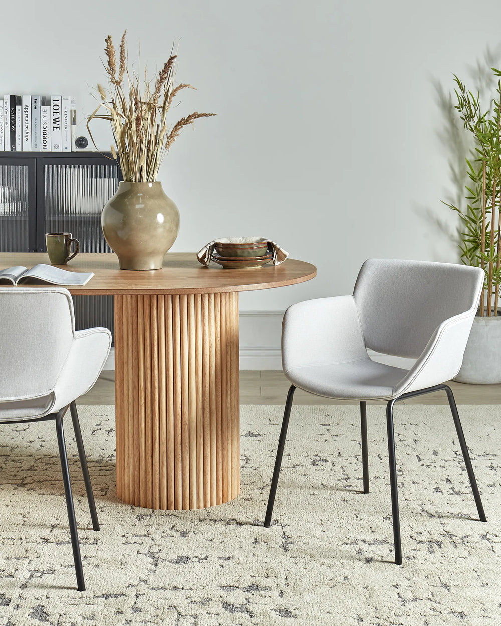 Light grey fabric dining chairs with integrated armrests and black metal legs around a dining table in a contemporary dining space with modern décor.