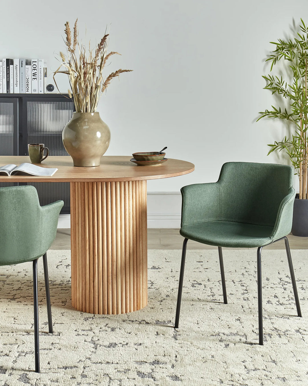 Green fabric dining chairs with integrated armrests and black metal legs around a dining table in a contemporary dining space with modern décor.