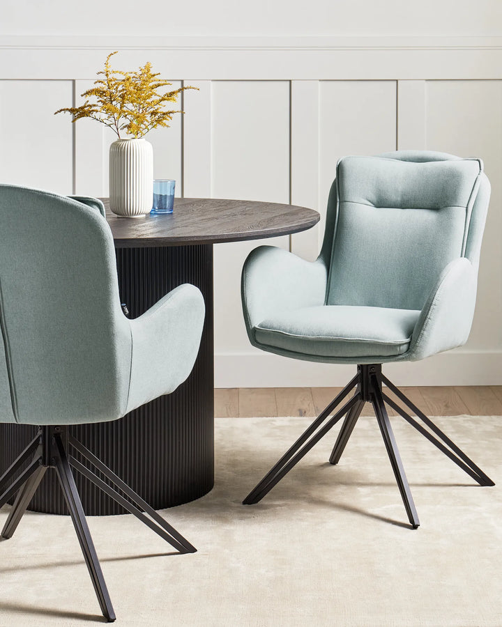 Modern dining area featuring light blue swivel chairs around a dark round pedestal table, creating a refined and inviting space with soft contemporary styling.
