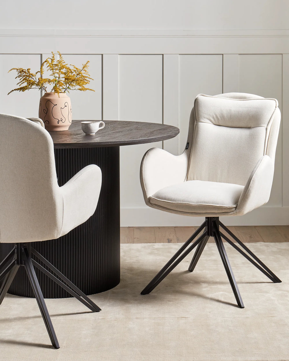 Elegant dining setting featuring upholstered swivel chairs around a dark fluted table, combining comfort, sophistication, and modern design.