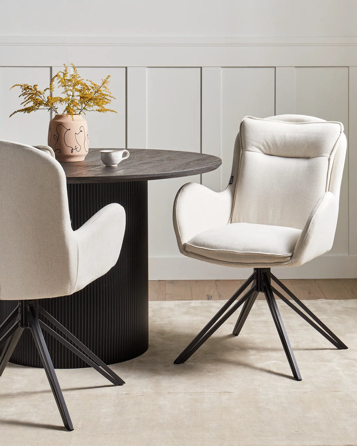 Elegant dining setting featuring upholstered swivel chairs around a dark fluted table, combining comfort, sophistication, and modern design.