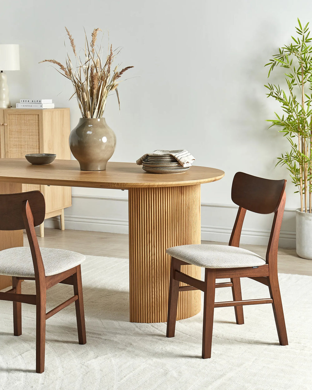 Dark wood dining chairs styled around a natural wood pedestal table in a calm, airy dining space, blending warm textures and earthy tones for a cozy, elegant, and contemporary atmosphere.