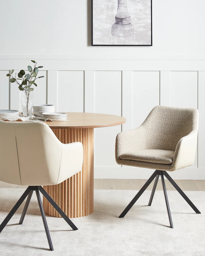 Taupe dining chairs with upholstered seats, faux leather backs, and black metal legs arranged around a dining table in a bright, modern dining space with minimalist décor.