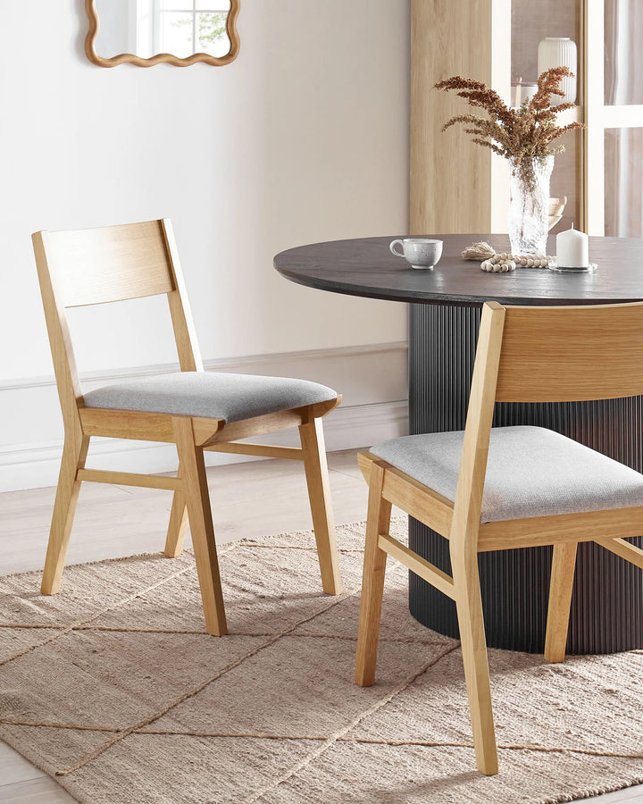 Light wood dining chairs styled around a dark round table, creating a warm contemporary dining space with soft neutral tones, textured fabrics, and an effortlessly modern feel.