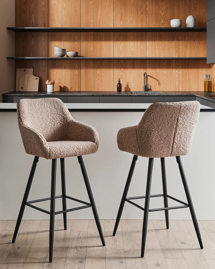 Taupe bouclé bar chairs with rounded backrests and slanted black metal legs around a bar counter in a contemporary kitchen or dining space with modern décor.
