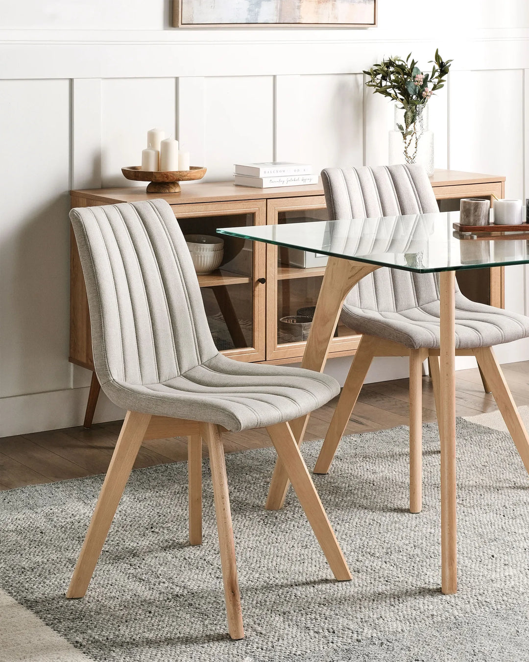 Bright Scandinavian-style dining space featuring upholstered chairs with wooden legs and a glass-top table for a clean, modern look.