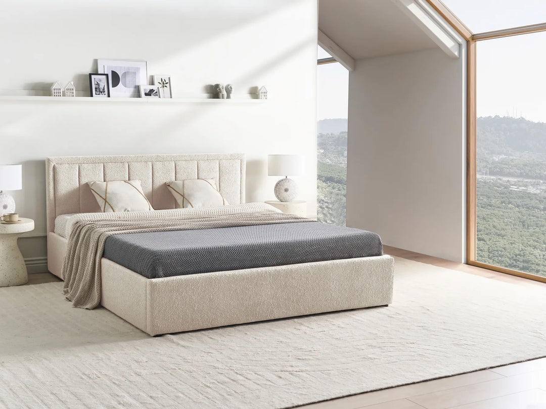 Beige upholstered bed in a modern bedroom with large windows.