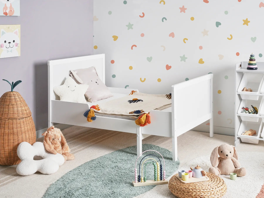 Children's bedroom with a white bed, colorful wall stickers, and toys on a light wooden floor.