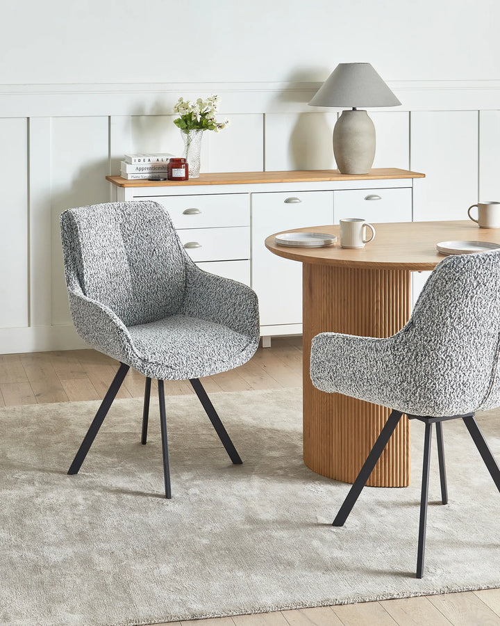 Black and white bouclé swivel dining chairs with metal legs around a dining table in a contemporary dining space with modern décor.