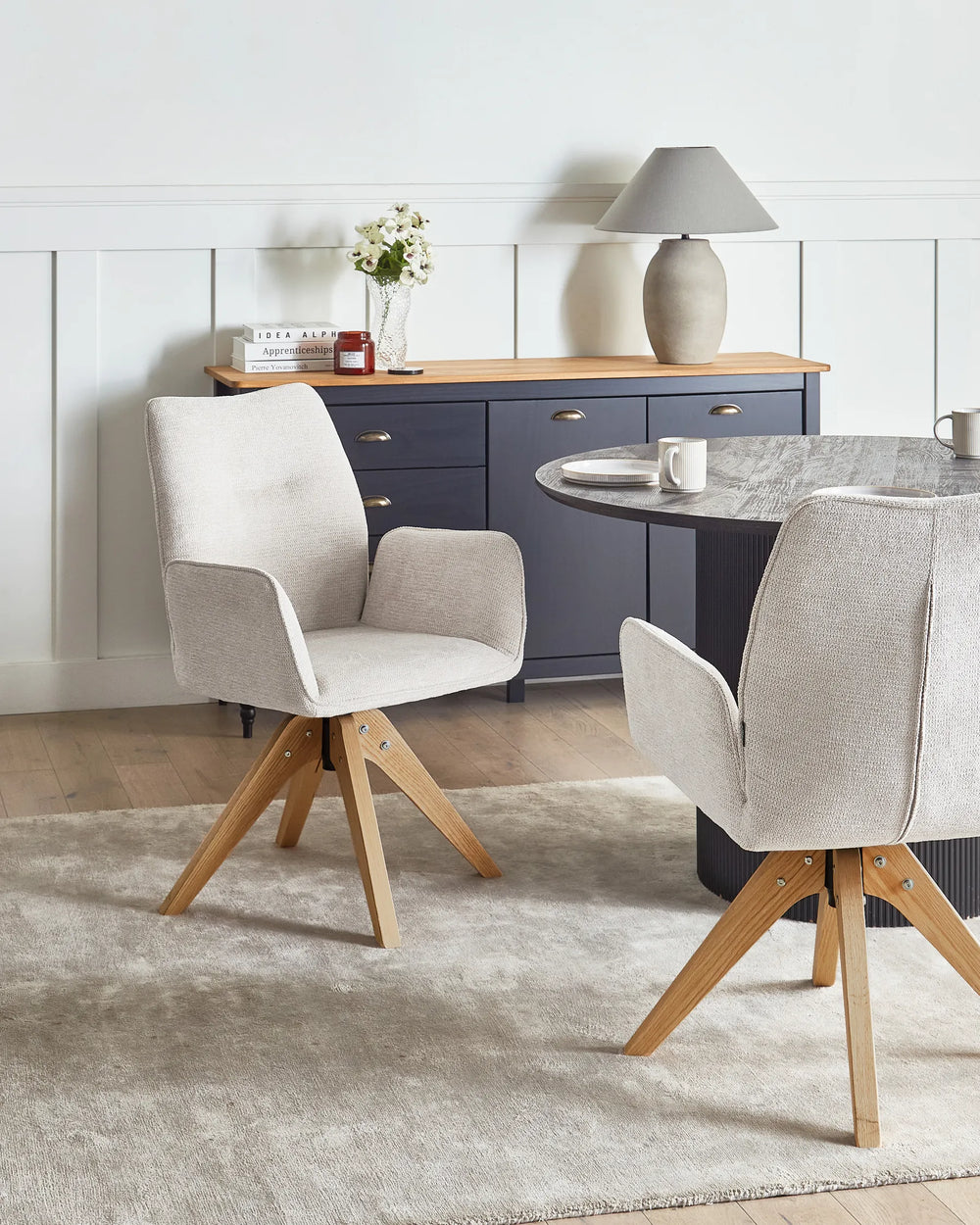 Light beige faux linen swivel dining chairs with oak legs around a dining table in a bright, Scandinavian-style dining space.