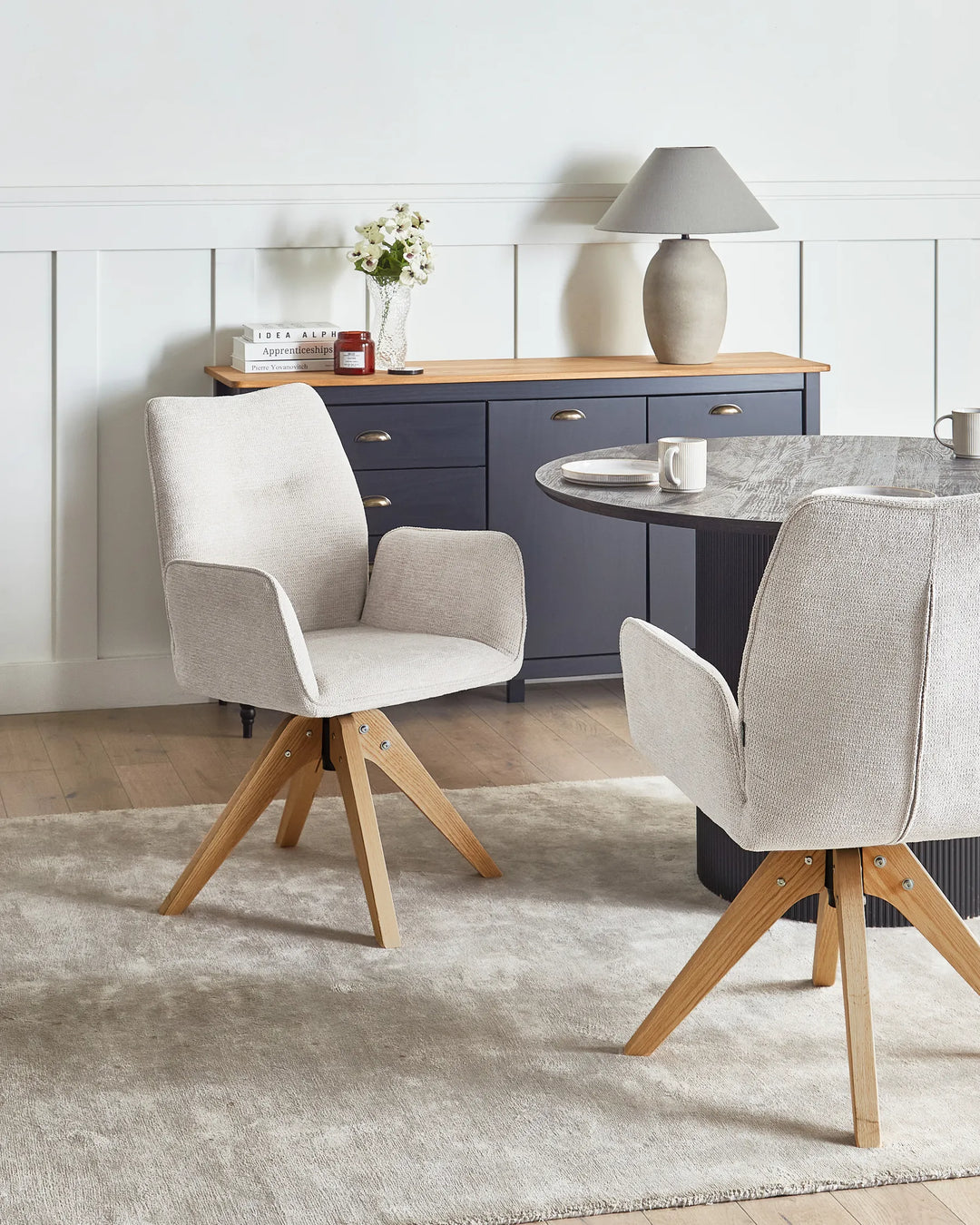 Light beige faux linen swivel dining chairs with oak legs around a dining table in a bright, Scandinavian-style dining space.