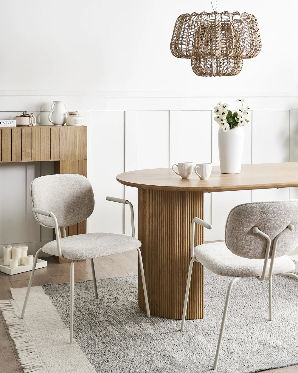 Light beige chenille dining chairs with curved backrests, integrated armrests, and black metal frames arranged around a dining table in a bright, modern dining space with minimalist décor.