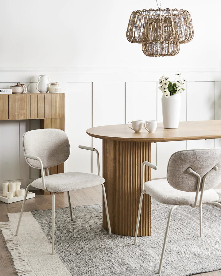 Light beige chenille dining chairs with curved backrests, integrated armrests, and black metal frames arranged around a dining table in a bright, modern dining space with minimalist décor.
