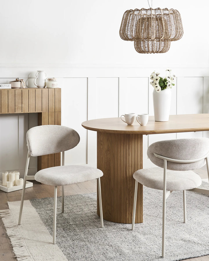 Cream bouclé dining chairs paired with a light wood dining table in a bright, modern dining room with a textured rug, wooden sideboard, and woven pendant light.
