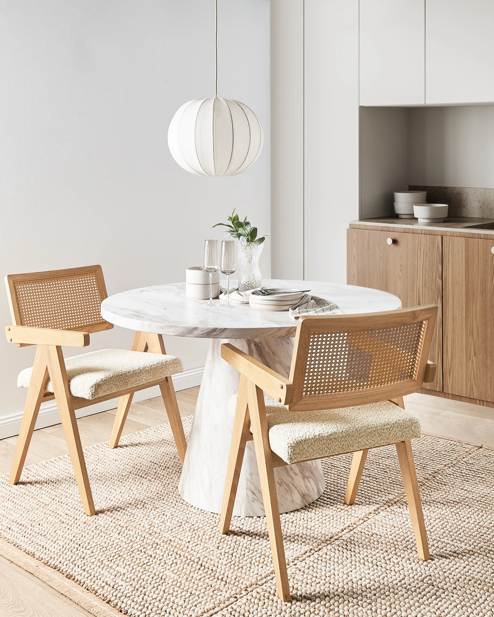 Light wood dining chairs with woven cane backrests and cream boucle seats around a round marble dining table in a modern dining room.