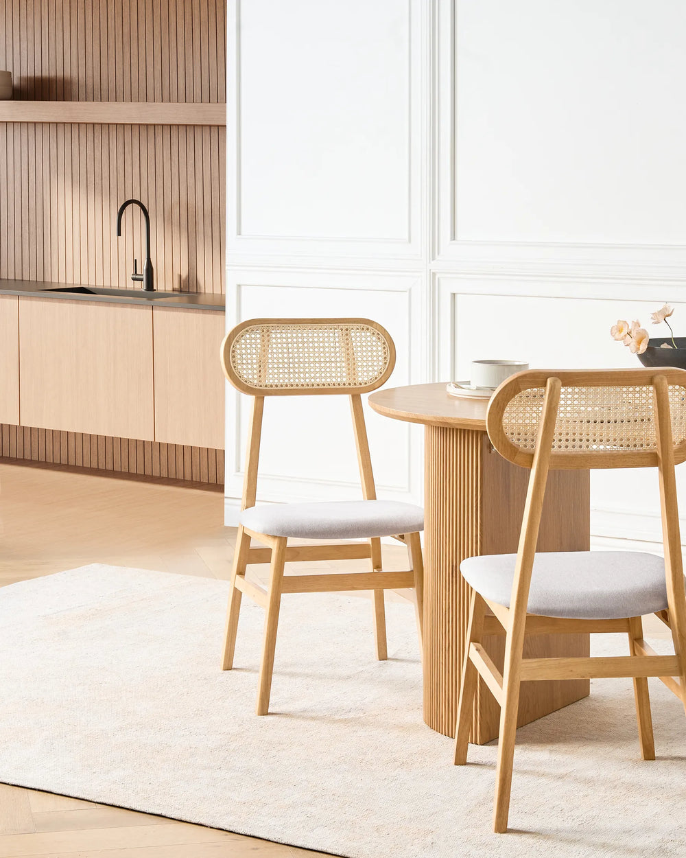 Light wood cane-back dining chairs styled around a round wooden dining table in a bright, modern dining space with neutral tones, soft textures, and warm minimalist décor.