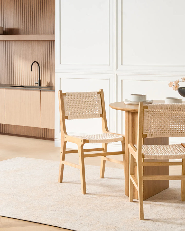 Light wood woven rope dining chairs around a wooden dining table in a bright modern dining room.