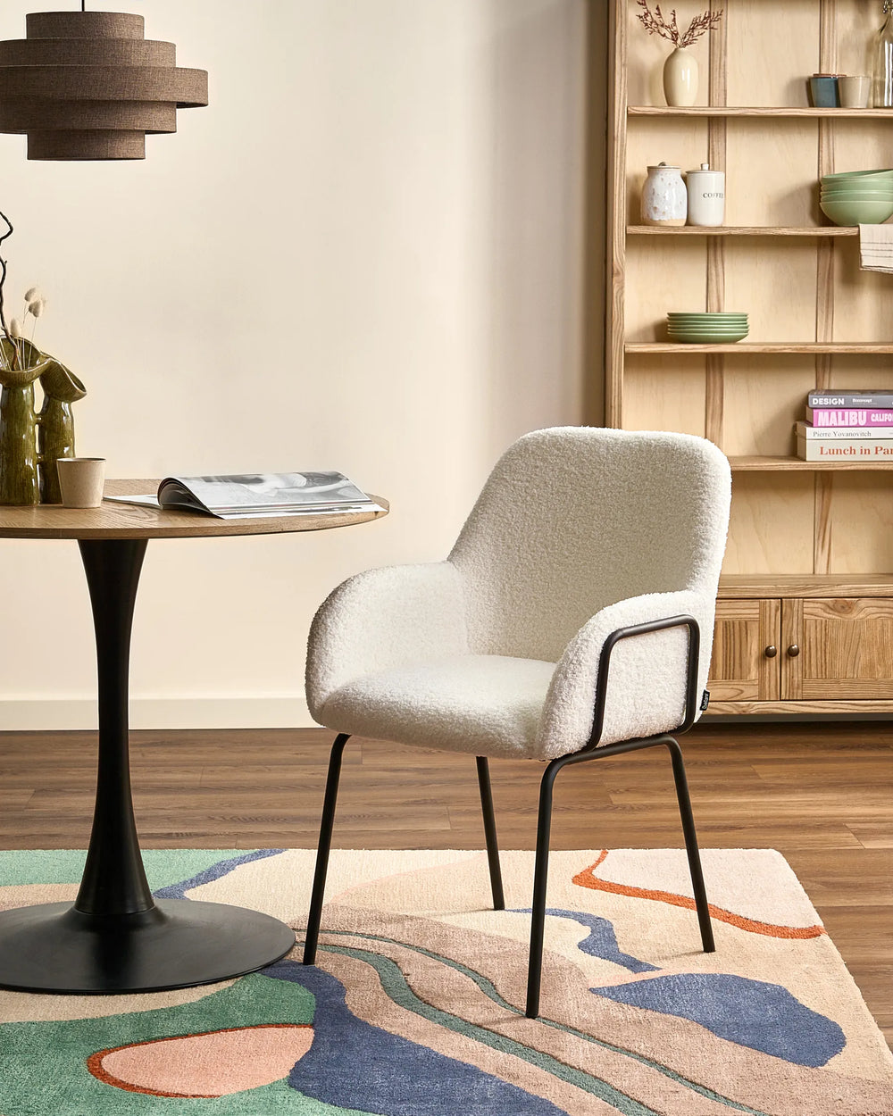 Off-white bouclé dining chairs with rounded backrests and black metal legs arranged around a dining table in a bright, modern dining space with minimalist décor.