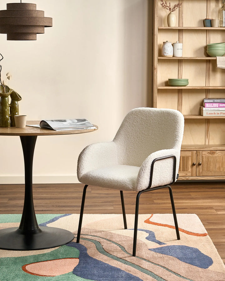 Off-white bouclé dining chairs with rounded backrests and black metal legs arranged around a dining table in a bright, modern dining space with minimalist décor.