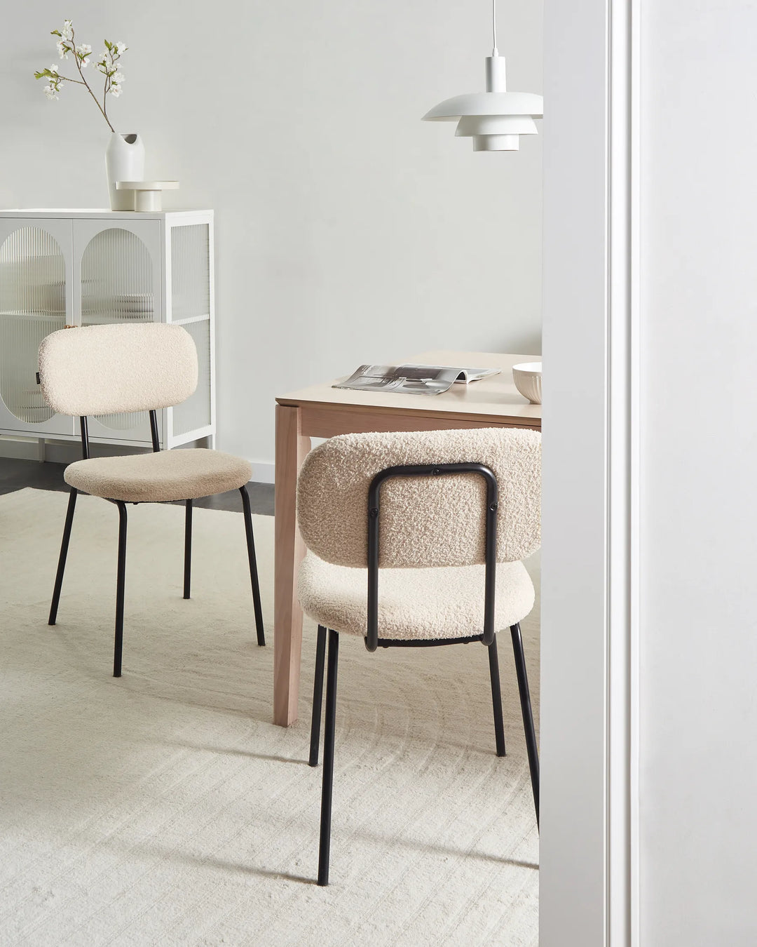 Beige bouclé dining chairs with curved backrests and black metal legs arranged around a dining table in a bright, modern dining space with minimalist décor.