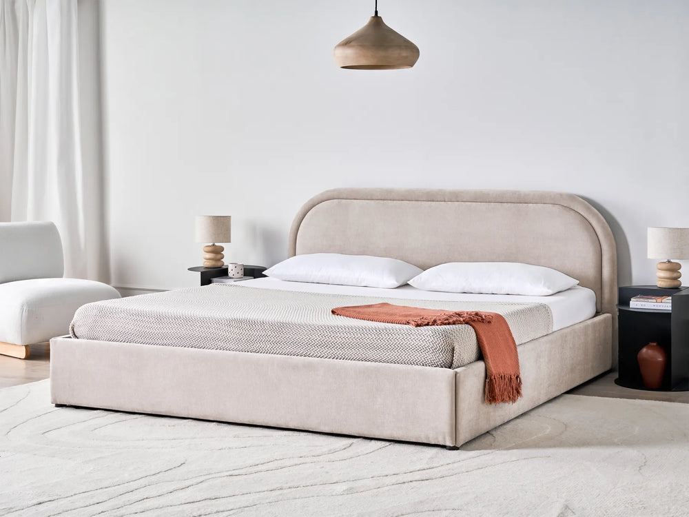 Beige upholstered bed in a modern bedroom with white walls and minimal decor.
