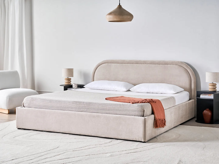 Beige upholstered bed in a modern bedroom with white walls and minimal decor.