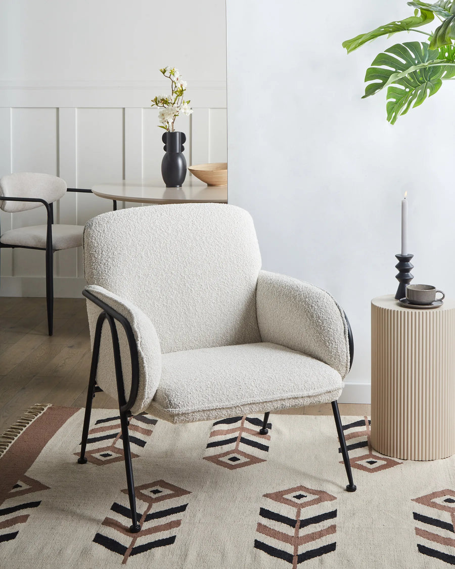 Beige armchair in a modern living room with a side table and decorative items.