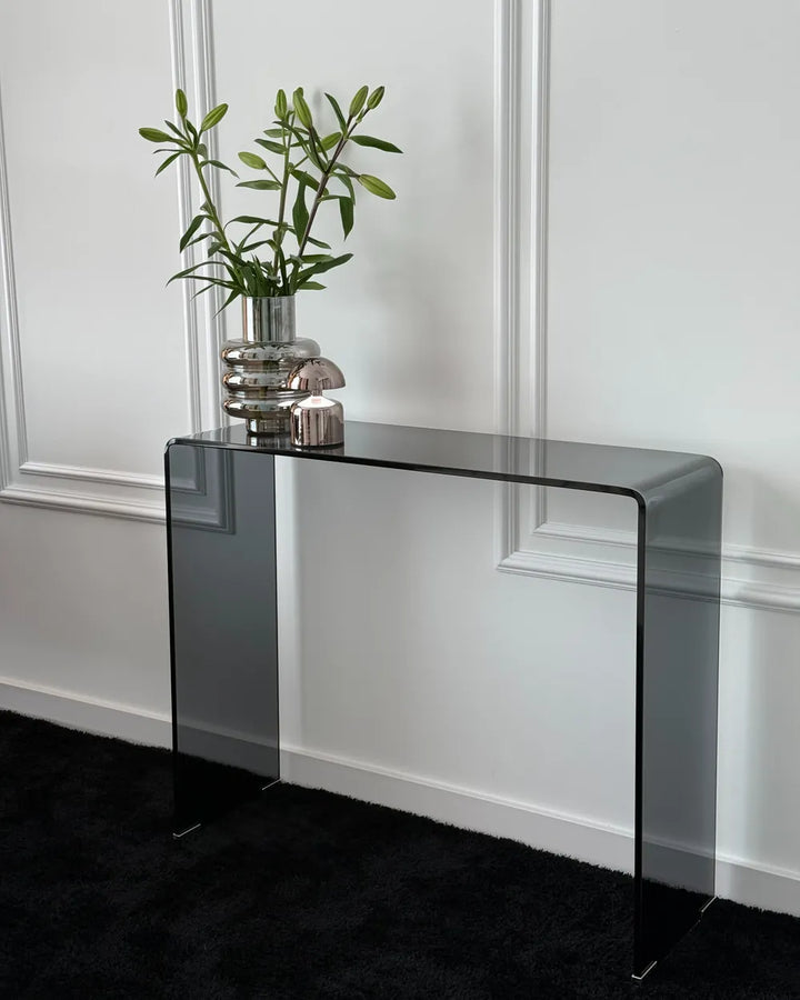 Glass console table with a plant and candle against a white wall.