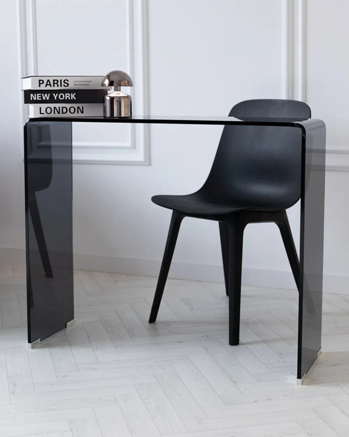 Black chair and table set against a white wall with books on the table.